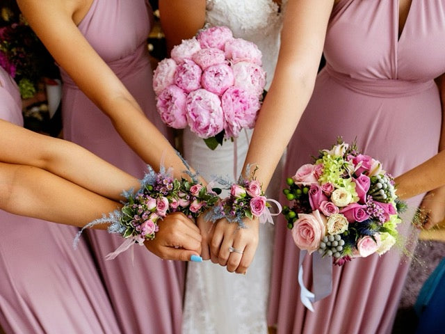 Bridesmaids in pink dresses holding bouquets and floral arm bands.