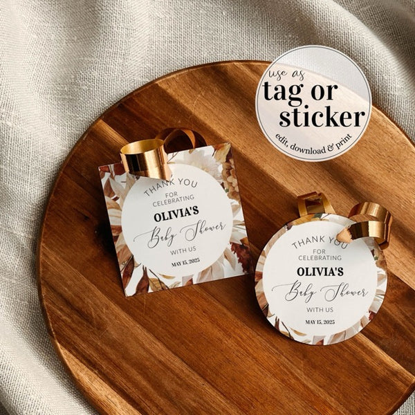 Round favor tags with gold ribbons on a wooden plate, featuring text for a baby shower.